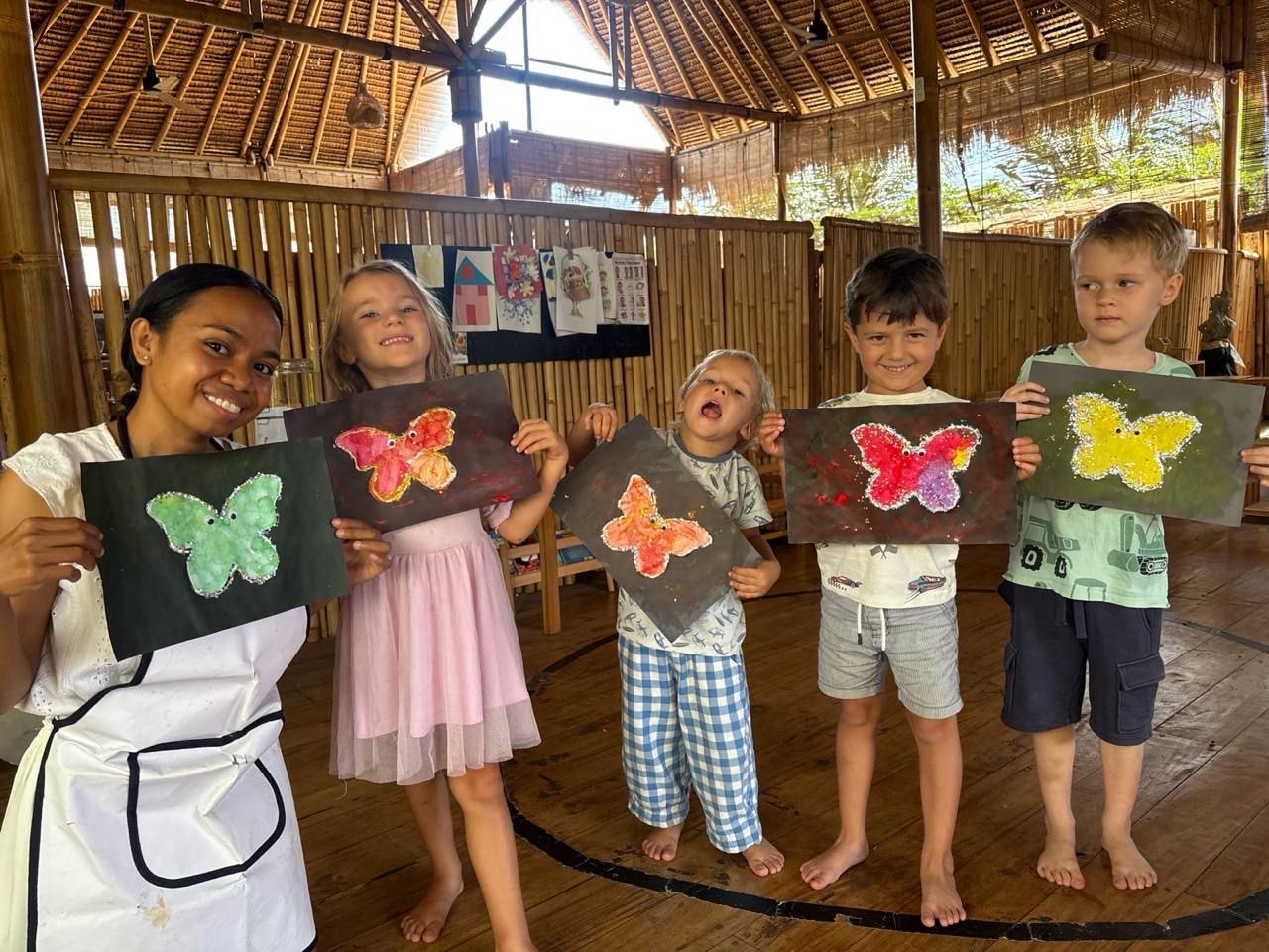 Niños mostrando con orgullo sus trabajos junto a su educadora en Balu Kids