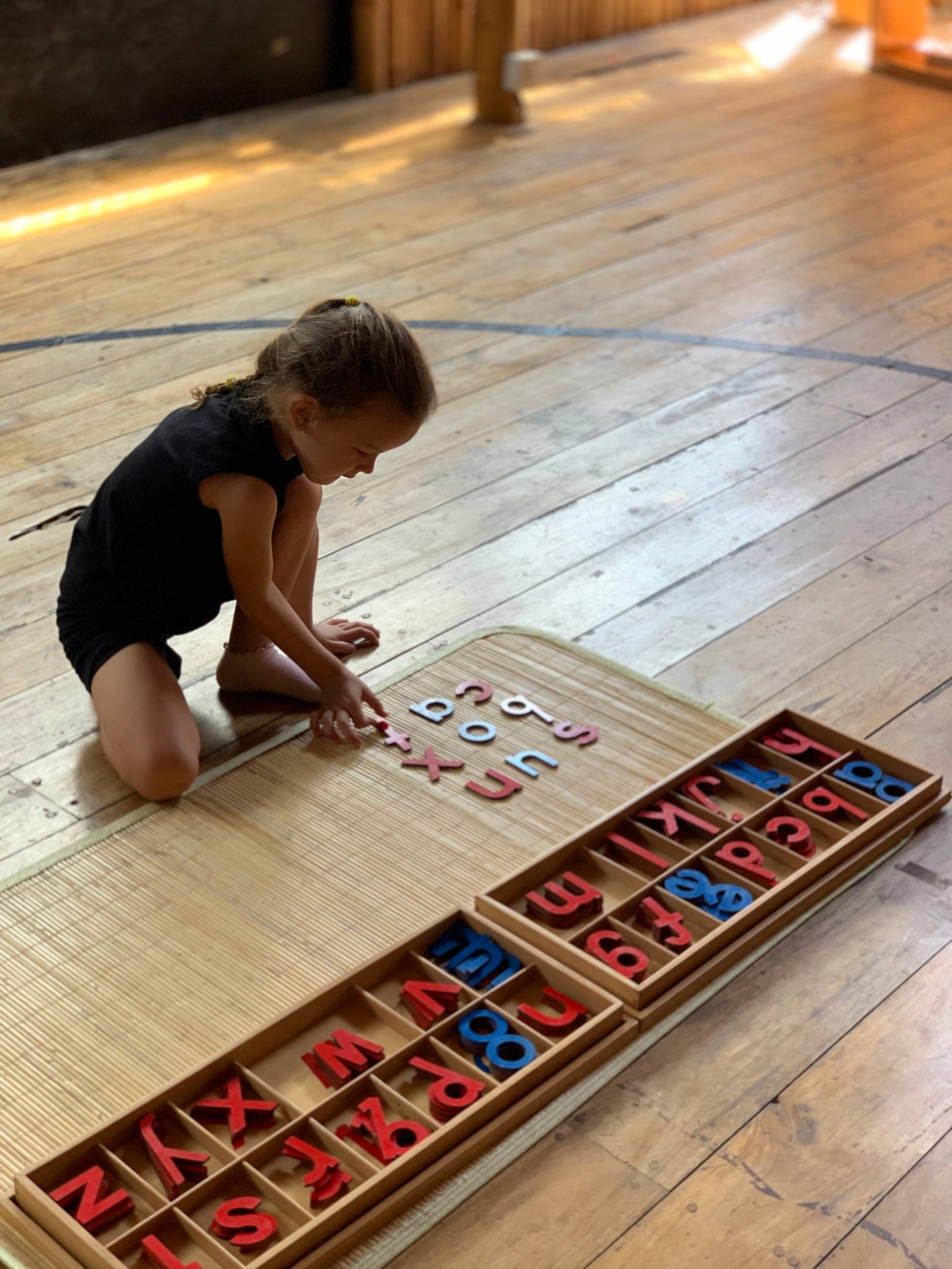 Un enfant dispose l'alphabet mobile Montessori sur le sol chez Balu Kids
